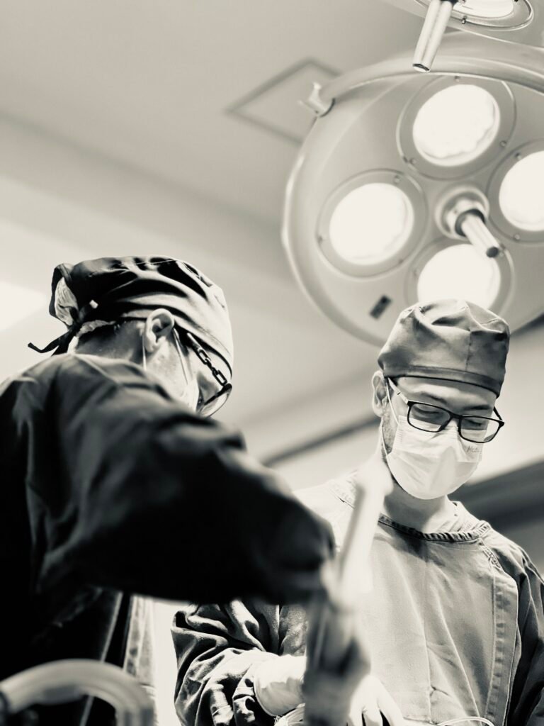 Dra. Izadora Reis e Dr. Lucas Cunha realizando uma cirurgia plástica de lipoaspiração (lipo HD) com um foco cirúrgico no fundo da fotografia.