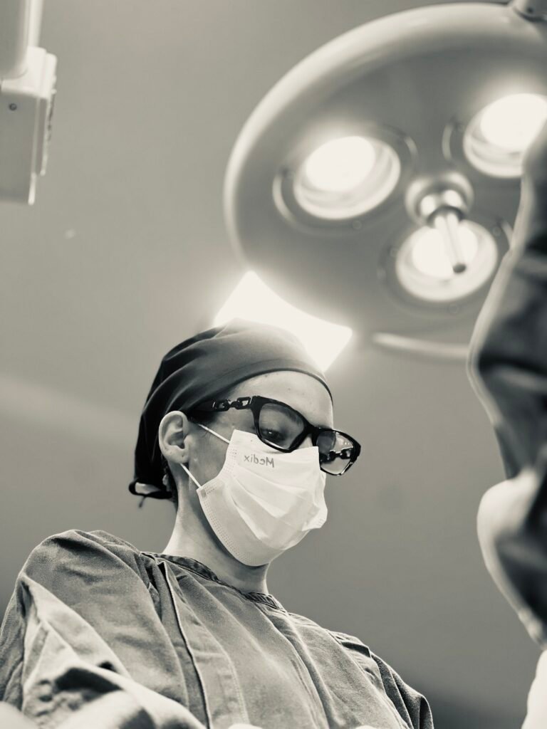 Dra. Izadora Reis concentrada ao realizar uma cirurgia plástica de abdominoplastia e lipoaspiração. Está no centro cirúrgico com foco de luz ao fundo.